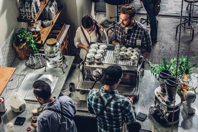 Two people buying a coffee at a hipster cafe while the baristas processing the order.