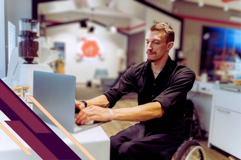 A white wheelchair using man at a co-working space and in front of a laptop.